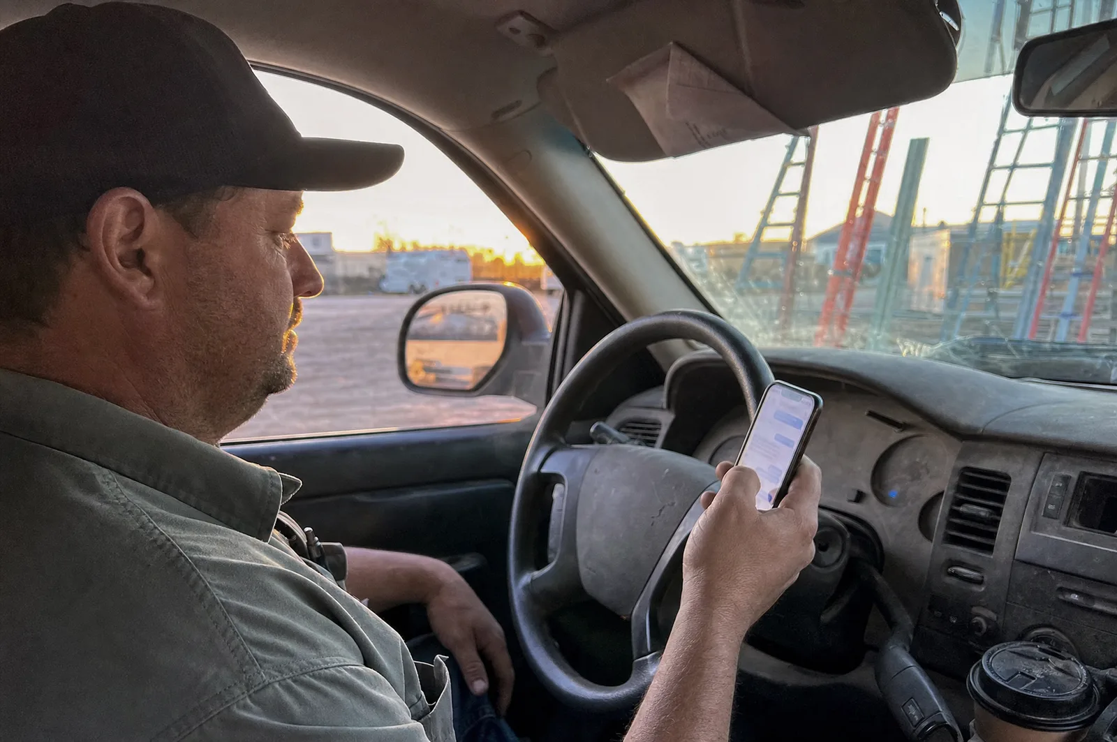 A contractor in his truck at golden hour, phone in hand, job site through the windshield